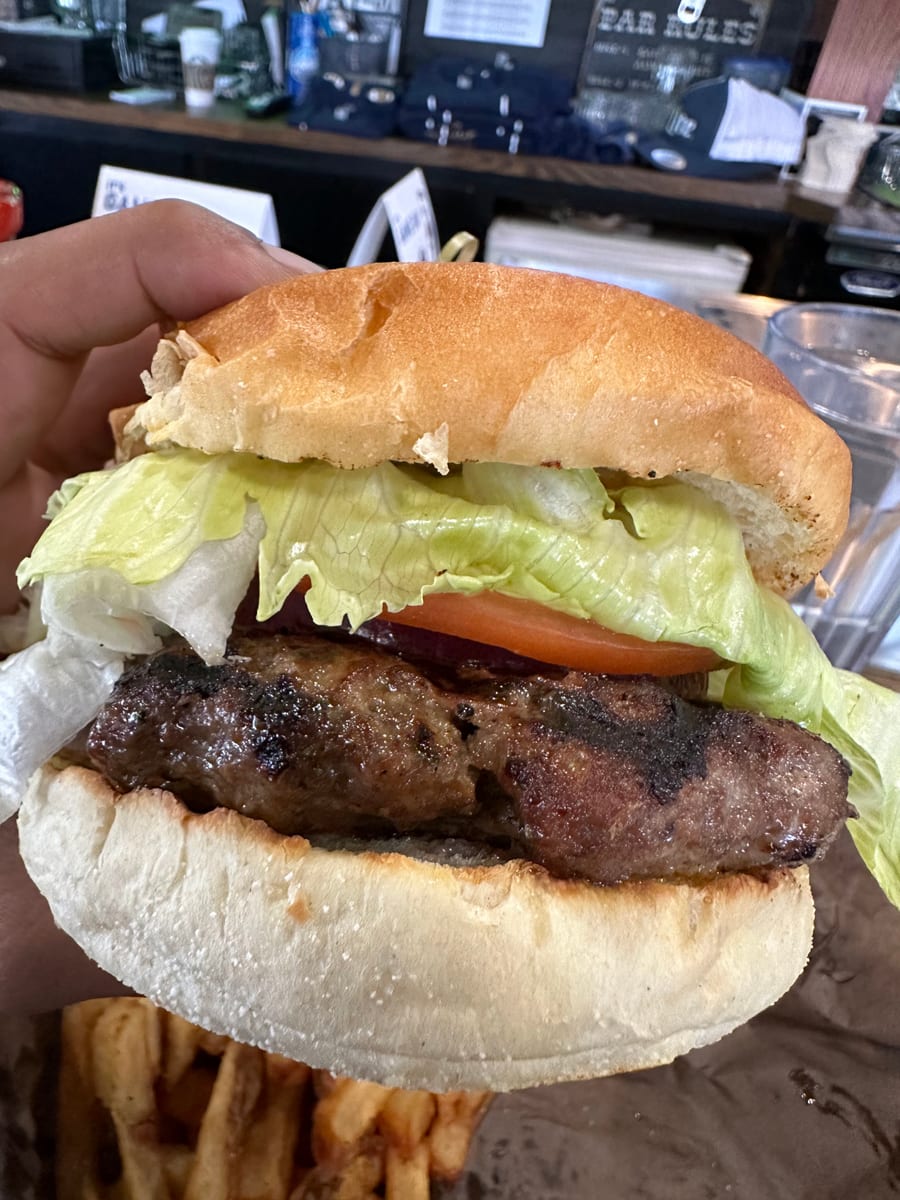 A burger with lettuce and tomato held over a plate of fries